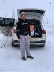 A student standing the snow in front of a white car with the trunk open