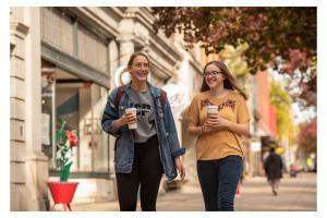 Two students walk along the shopfronts of Downtown York on a pleasant fall day, cups of coffee in hand.