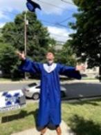 A student in his royal blue graduation cap and gown throwing his cap in the air