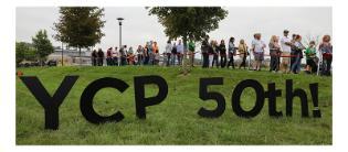 People gather outside during the 50th anniversary celebrations. A lawn sign spells out YCP 50th in large letters