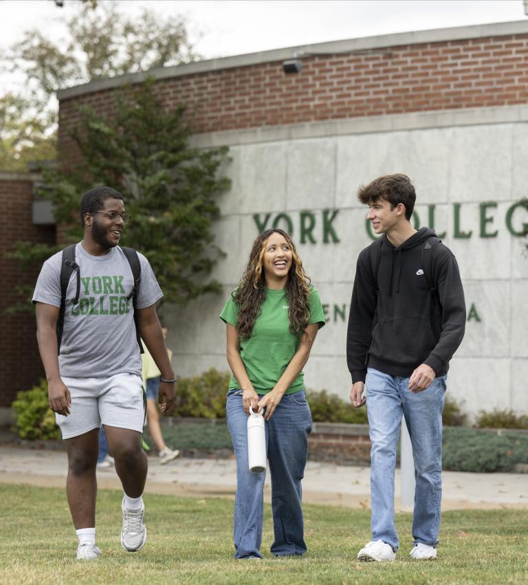 Three students walking together in front of a York College sign