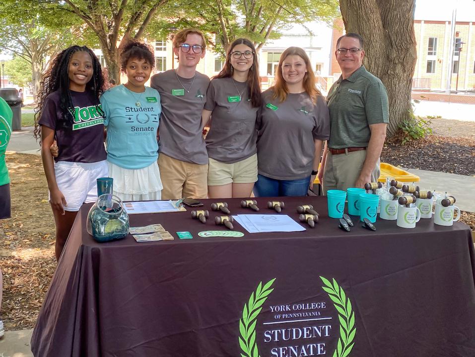 A group of five student senators pose by their involvement fair table with President Thomas D. Burns.