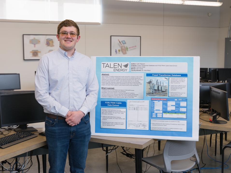 A student stands next to his poster presentation in a classroom.