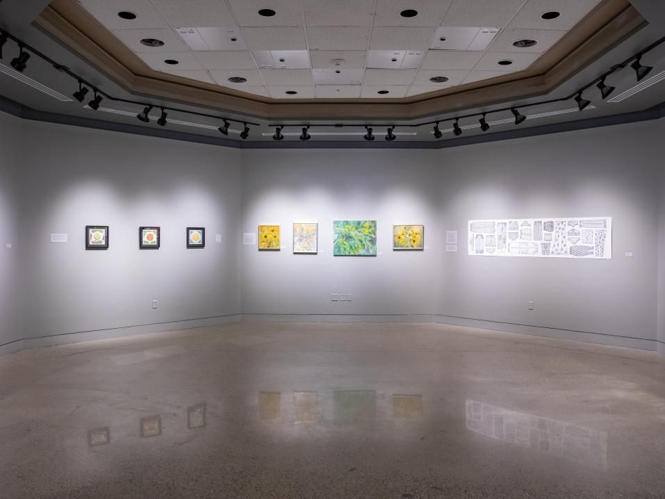 A large open room with art well lit on each wall of an octogonal space.