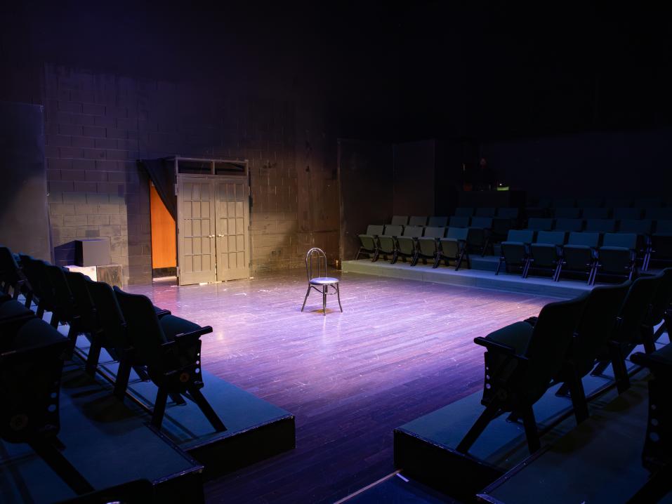 An empty theatre with a chair spotlighted in the middle of a stage.