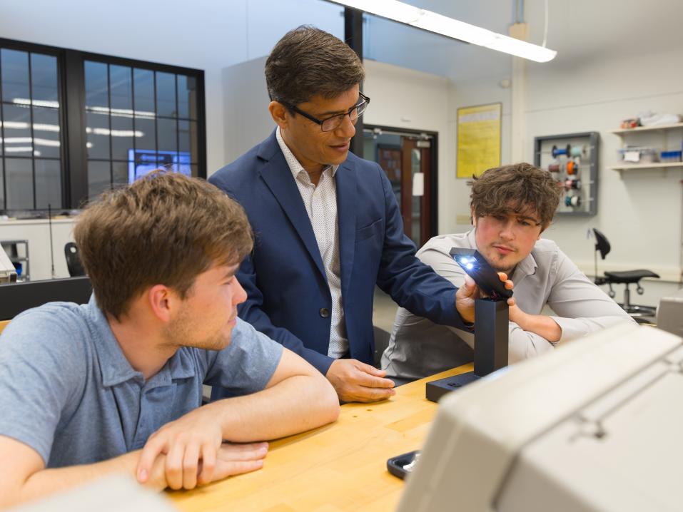 College students with a professor examine a light engineering project in a lab.