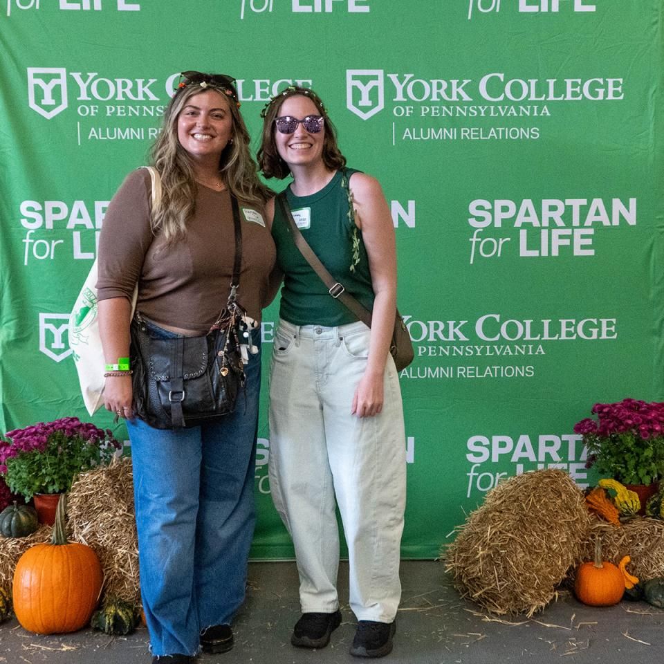 Two women stand together in front of a photo backdrop at Homecoming