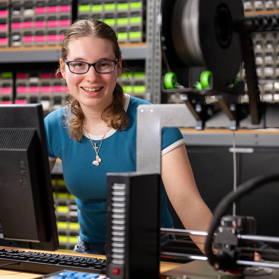 A student smiles at the camera as she works on technology