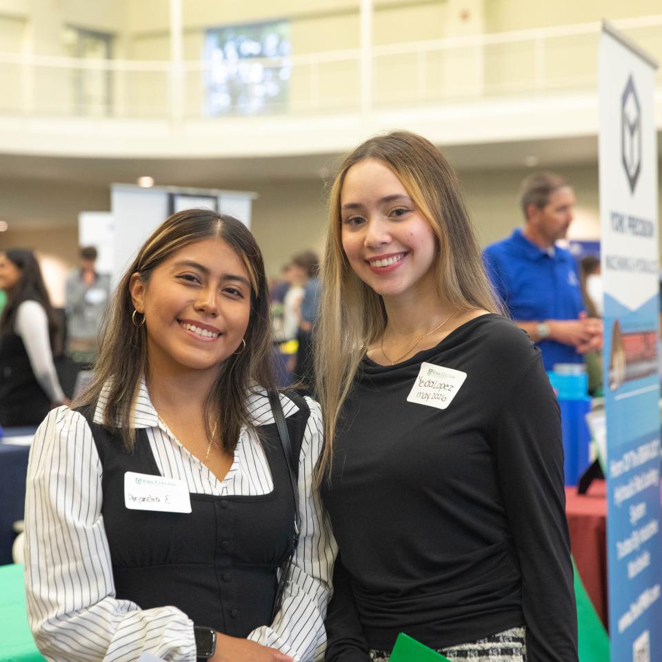 Two students in professional attire smile at the camera at a networking event.