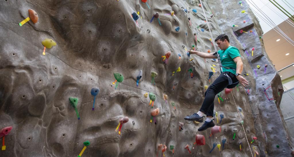 A student in a green shirt climbs an indoor rock wall