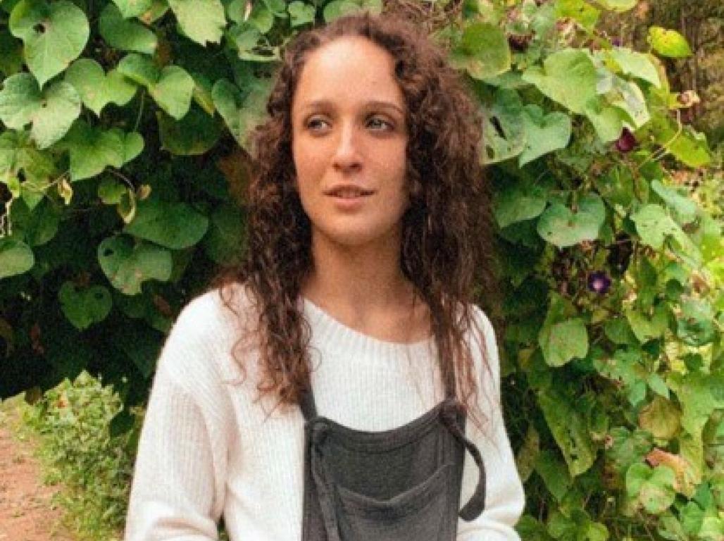 Bella Nace poses for a photo by greenery outdoors.