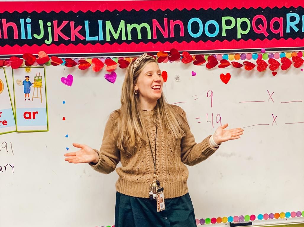 Brianna Weaver is teaching at the front of a classroom with math problems behind her on a whiteboard