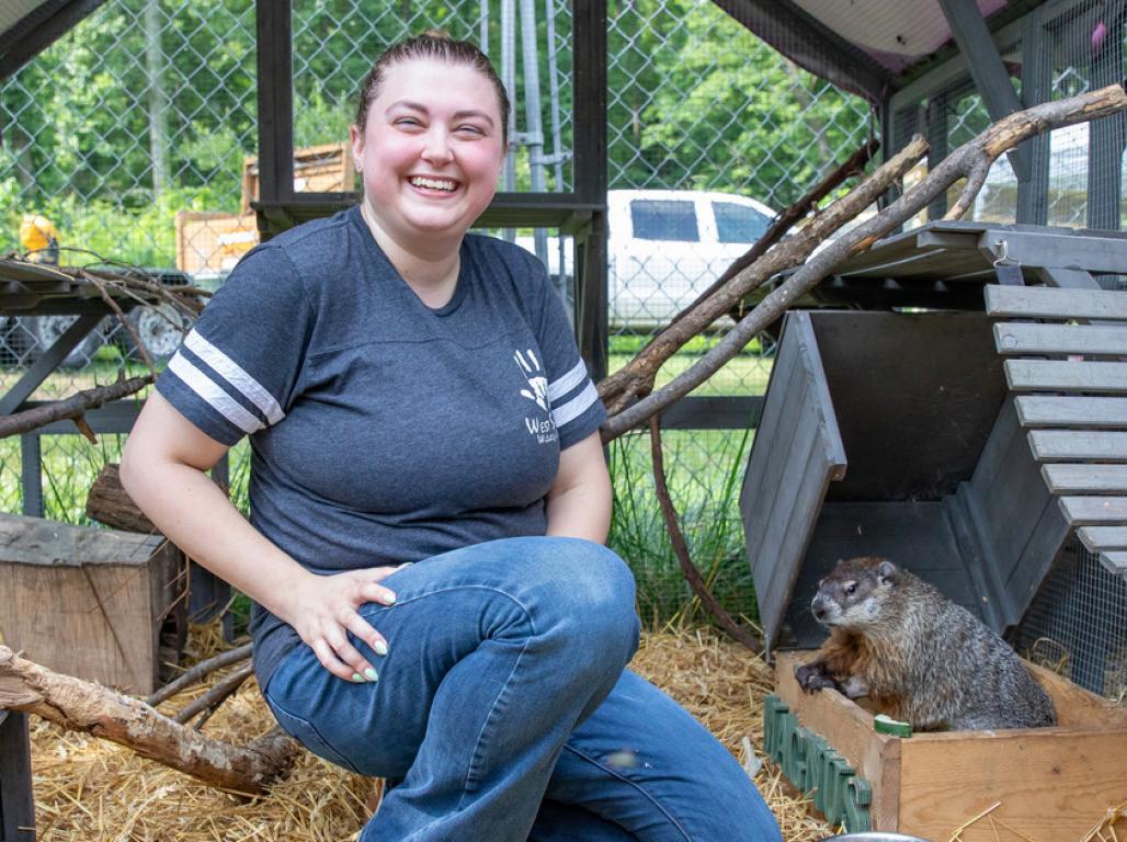 Emily Garrigan posing with a groundhog in an outdoor animal enclosure.