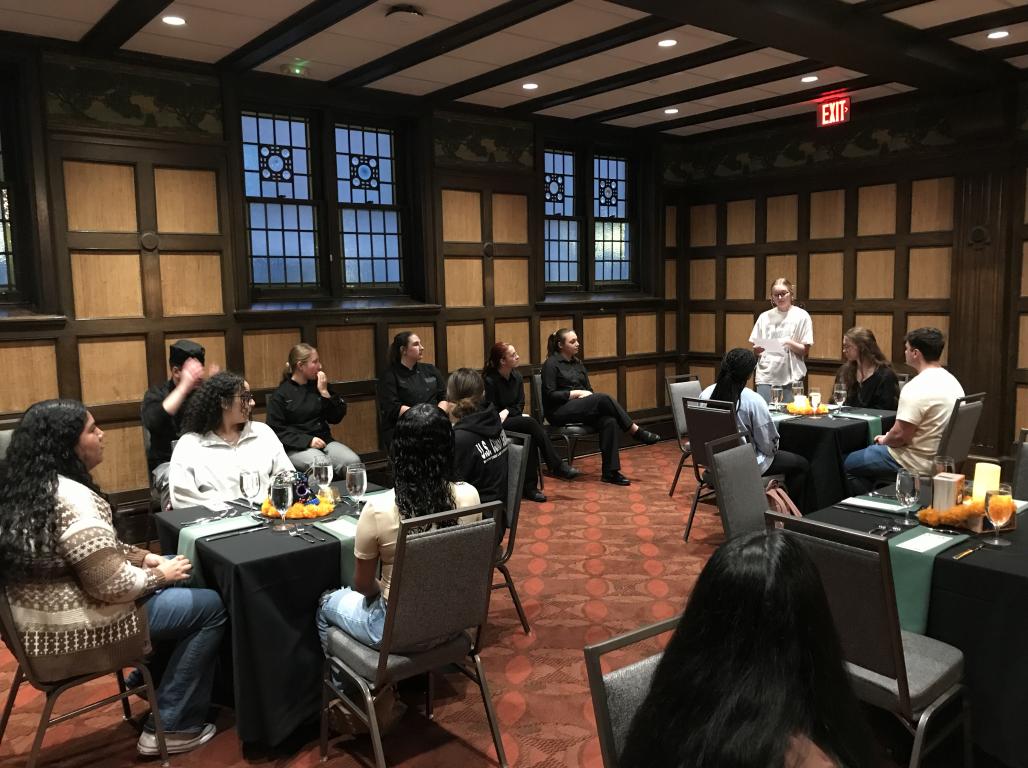 People seated at dining tables listening to someone speaking.