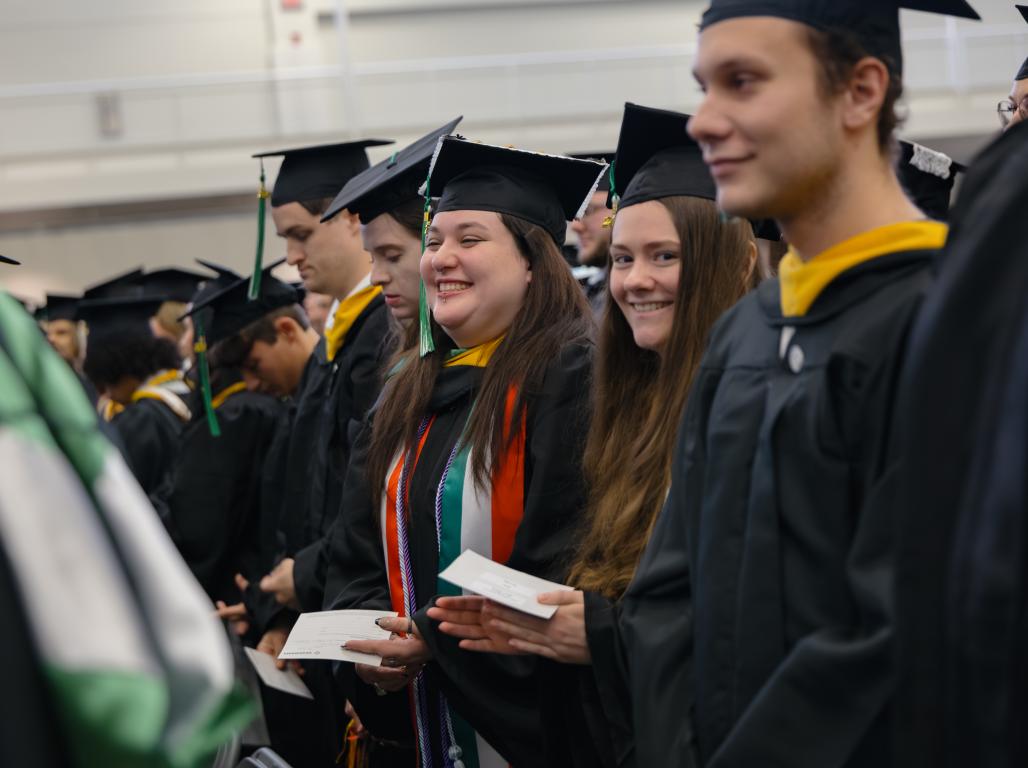 Graduates in regalia at their commencement ceremony, one is smiling at the camera.