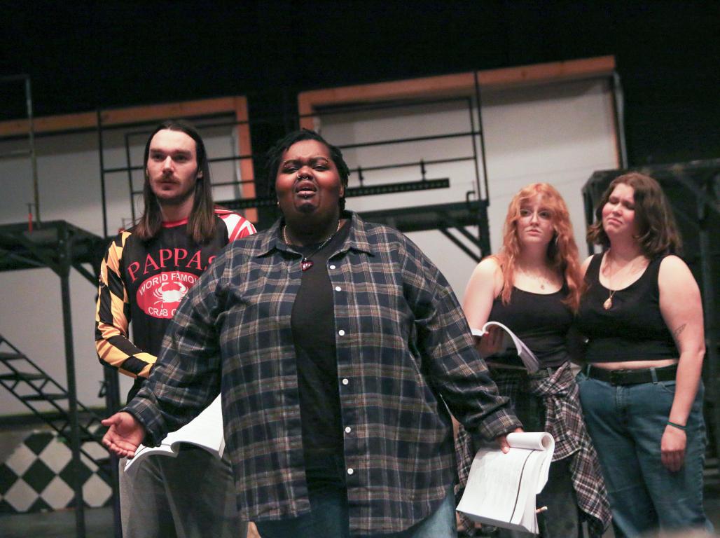 A group of college students performing on a stage. The performer in front appears to be singing.