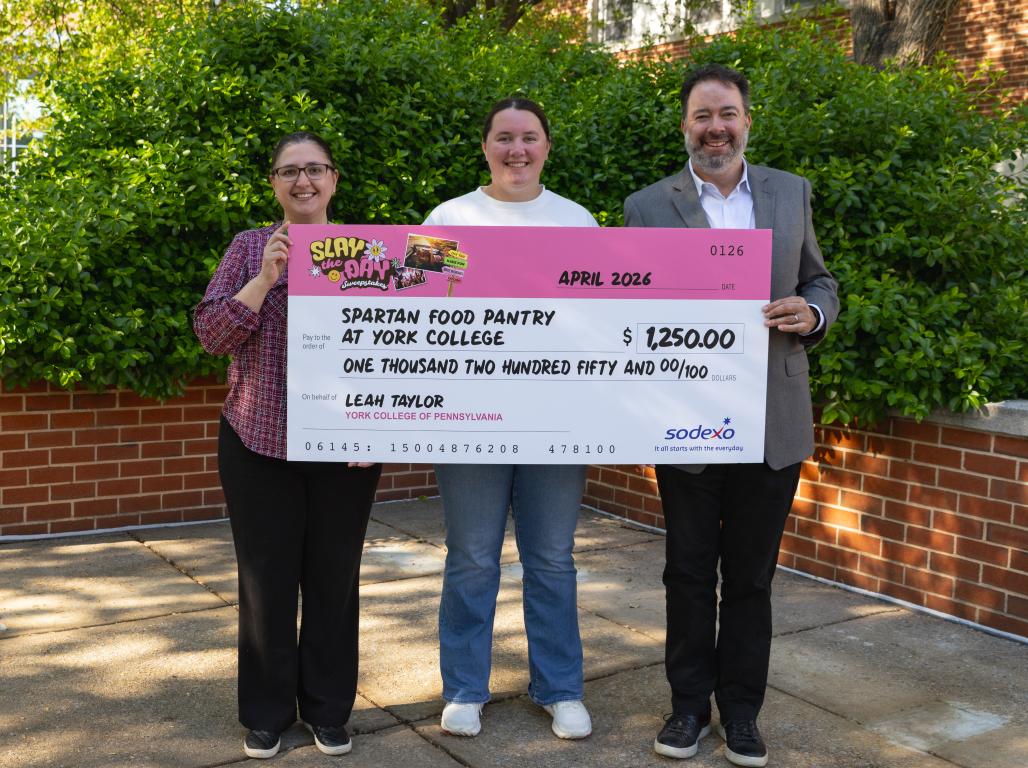 Three people posing with a large, ceremonial check made out to the Spartan Food Pantry of York College in the amount of $1250.