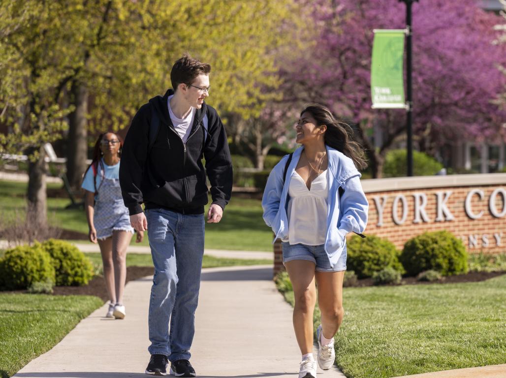 Students walking outside in spring with the York College sign behind them.