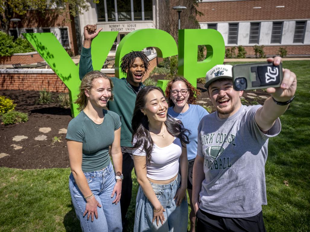 A group of students smile and pose for photo at YCP letters