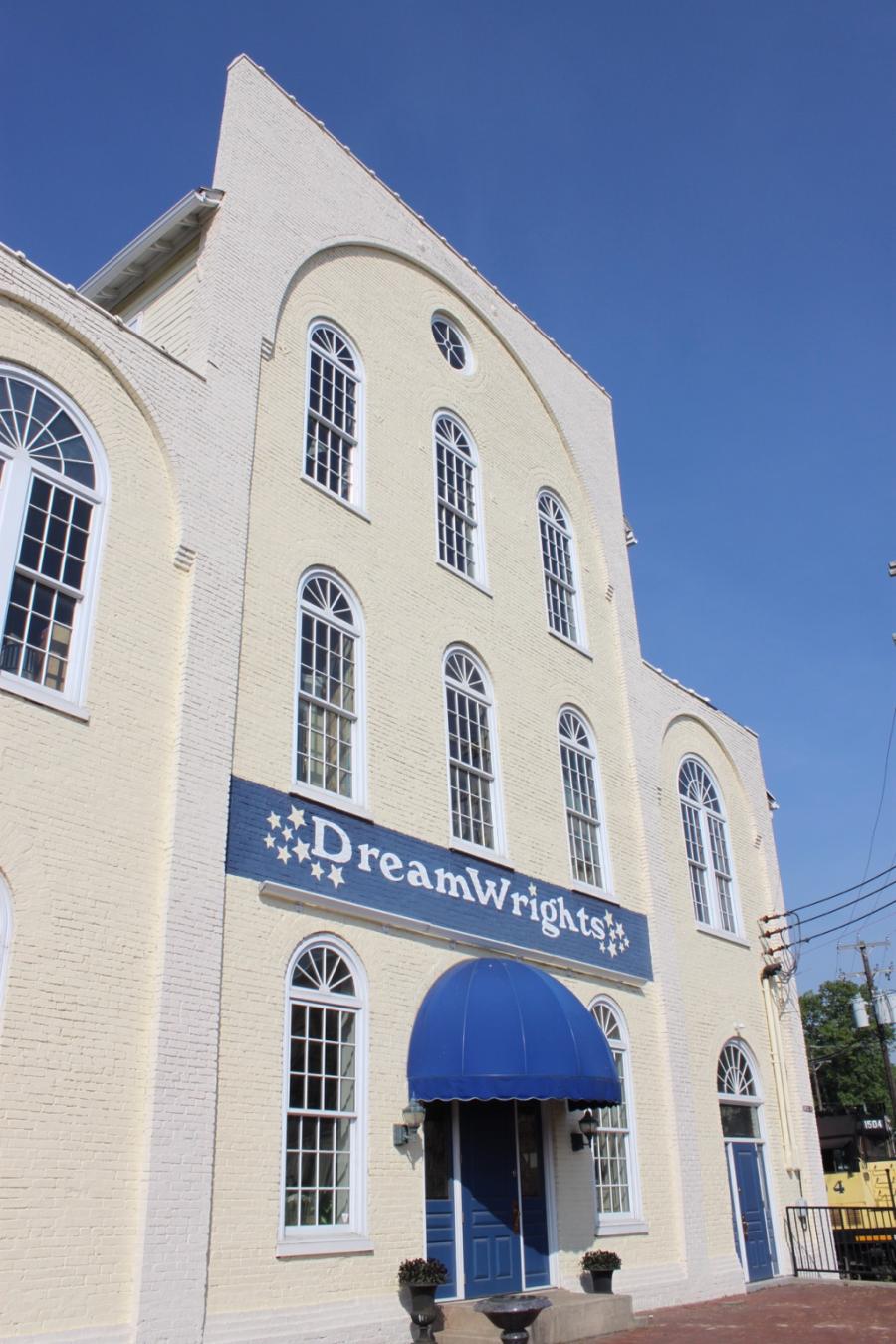 Exterior of a large, white building on a sunny day with a blue sign reading "DreamWrights."