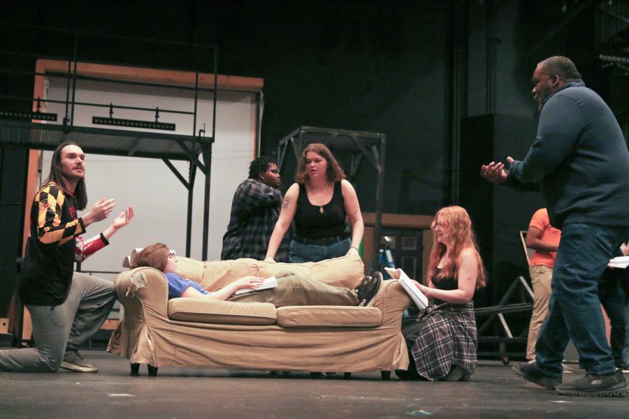 Rehearsal of a stage performance. The cast appears to be taking instruction from a director, all on a theatrical stage.