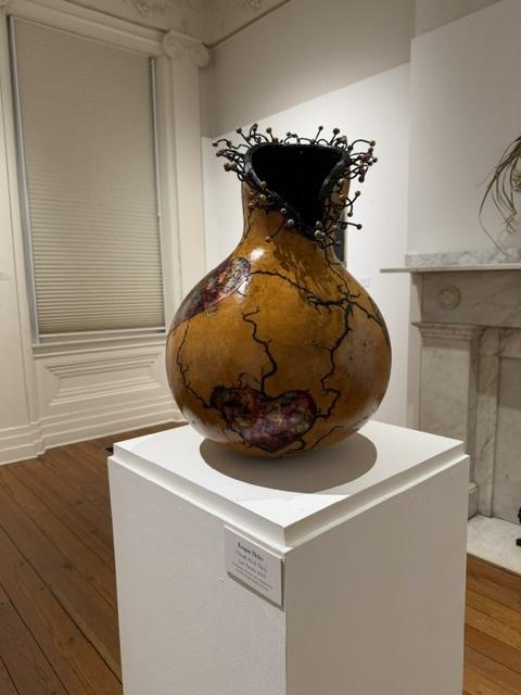 An artisanal clay jar on display in a gallery setting.
