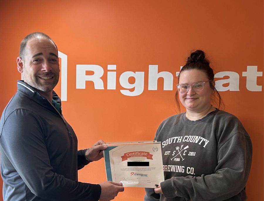 Dominic Cole presents a certificate to a woman standing in front of an orange wall that reads Right at Home