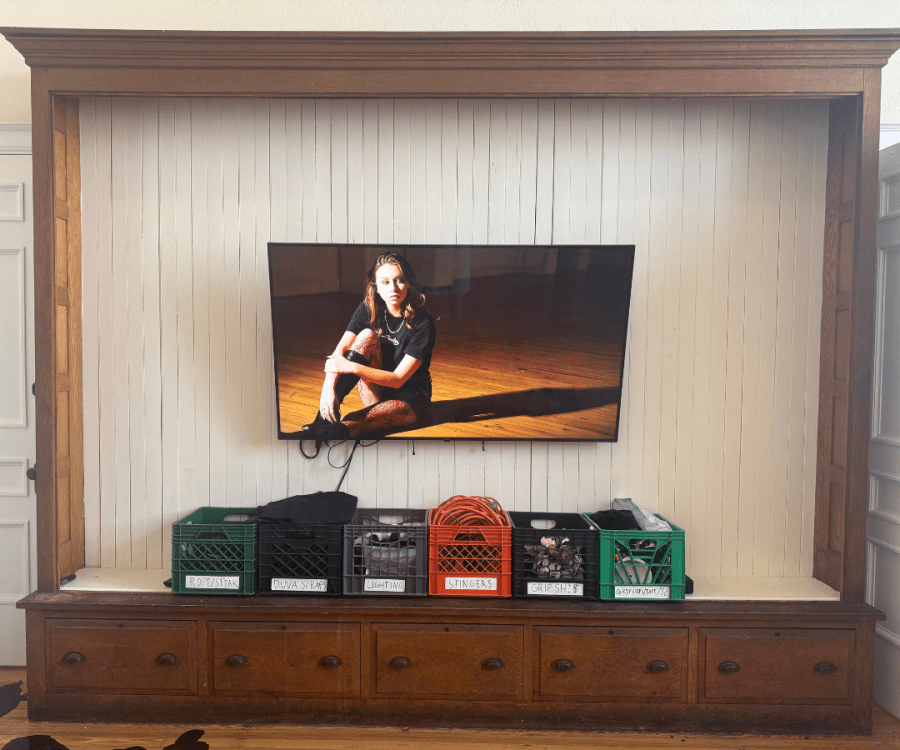 A video screen displays a film still above labeled production crates holding items such as rope, lighting equipment, and grip supplies.