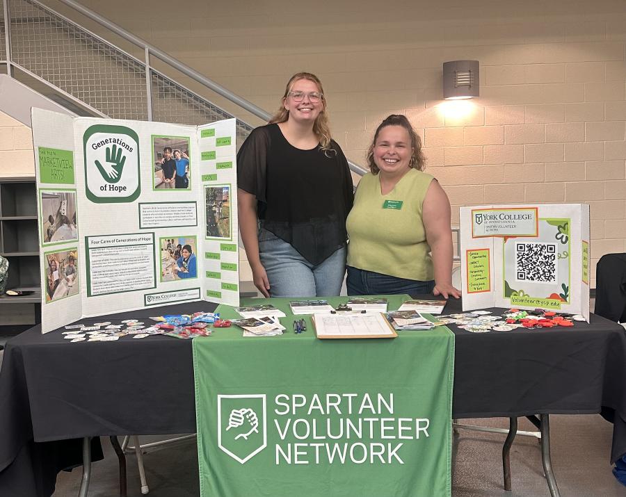 Khora Pawelczyk ’26 stands with another York College student behind a Spartan Volunteer Network table featuring Generations of Hope and volunteer engagement materials.