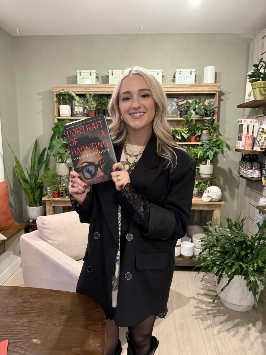 Madison Nelson holds her book in a shop with plants behind her.