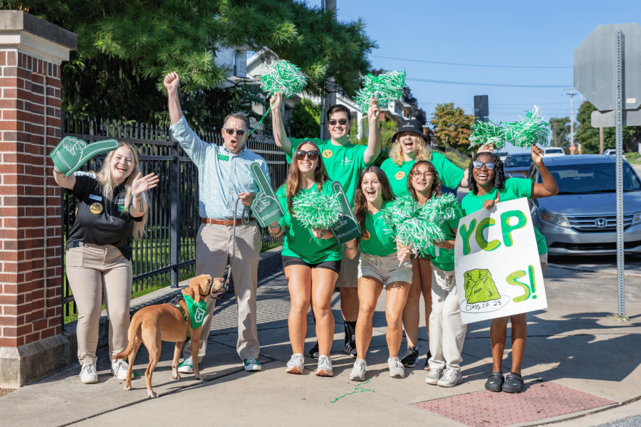 A group of York College students and staff cheer with pom-poms, foam fingers, and a YCP sign during Move-In Day.
