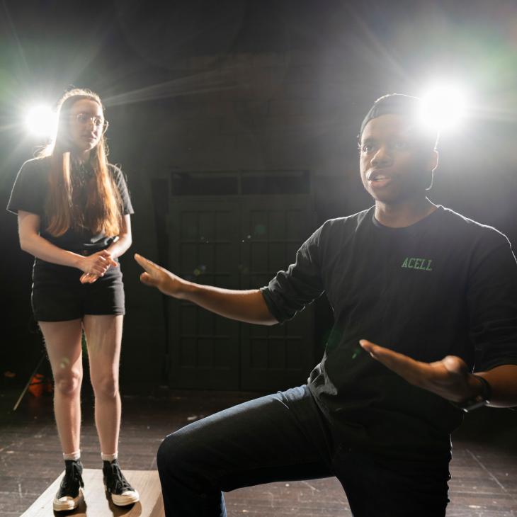 Students perform in the black box theater, backlit by dramatic theatre lighting. 