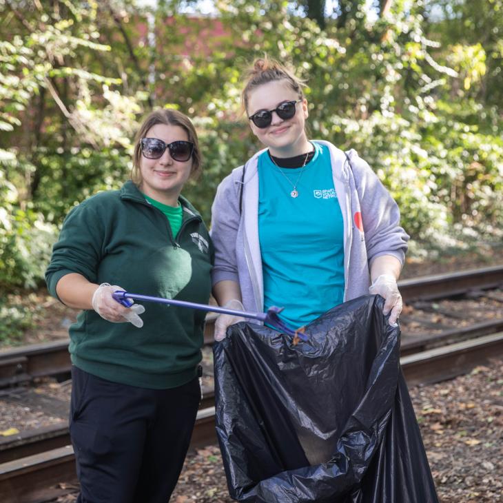 An Eisenhart Scholar student stand with another student holding a trashbag while clean up the railtrail