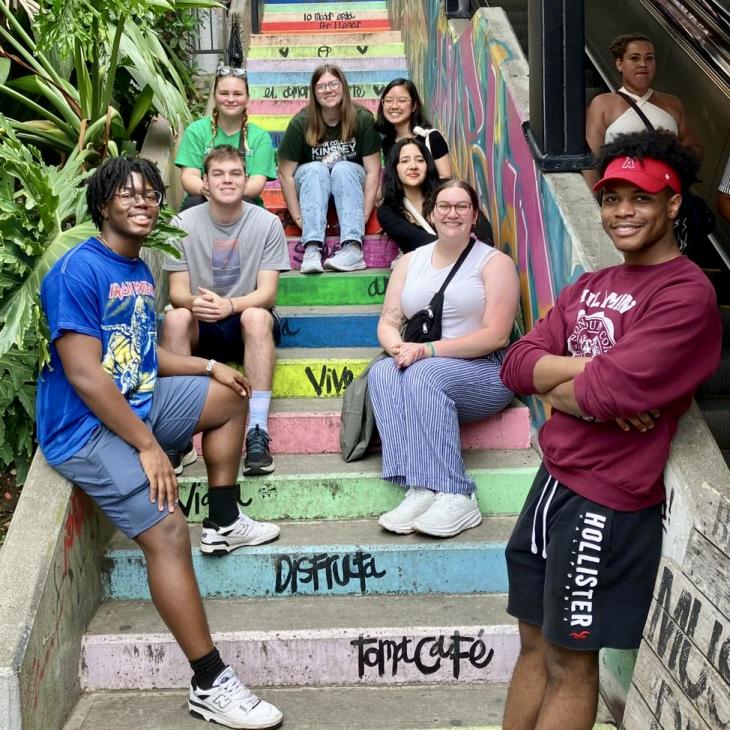 A group of students sit on colorful stairs in Columbia