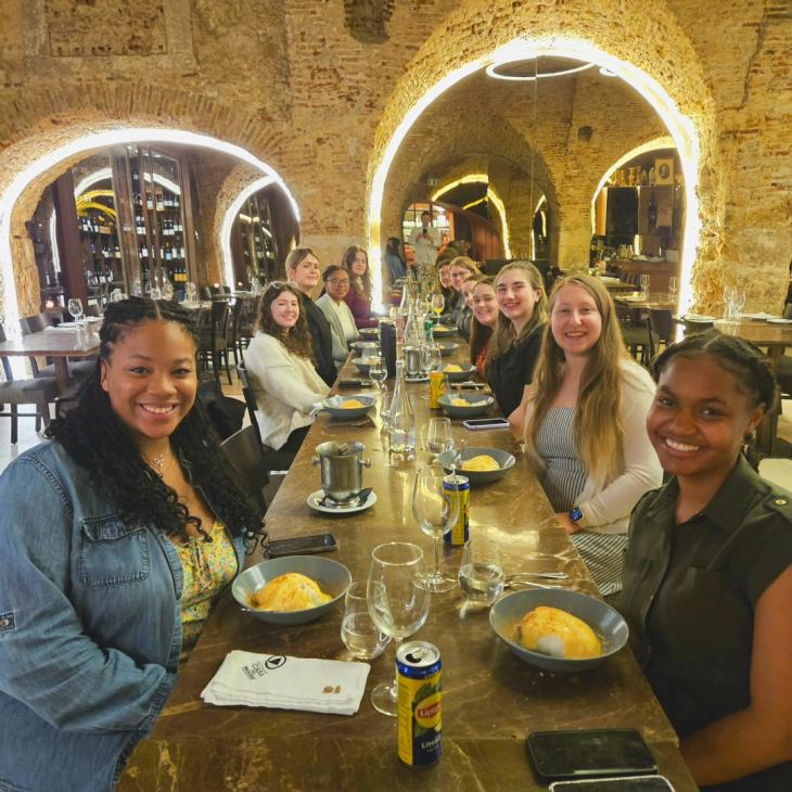 A large group of students sit at a table in Portugal smiling at the camera