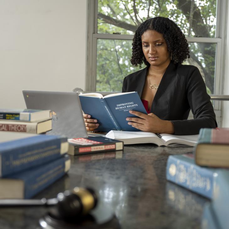 Person wearing a black blazer reading a book titled "Improving Human Rights." Other books and a gavel are visible on the table.