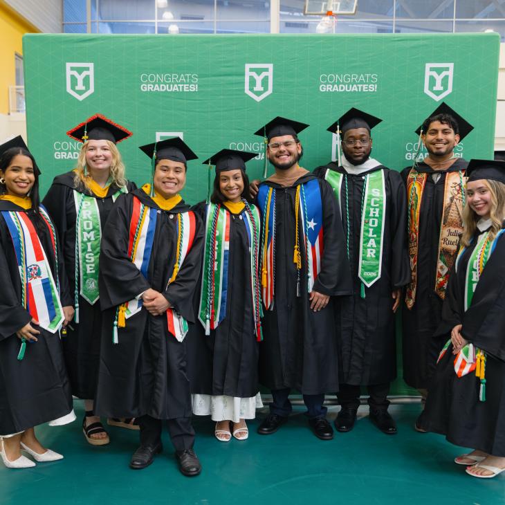 A group of students in caps and gowns stand together for a photo at graduation