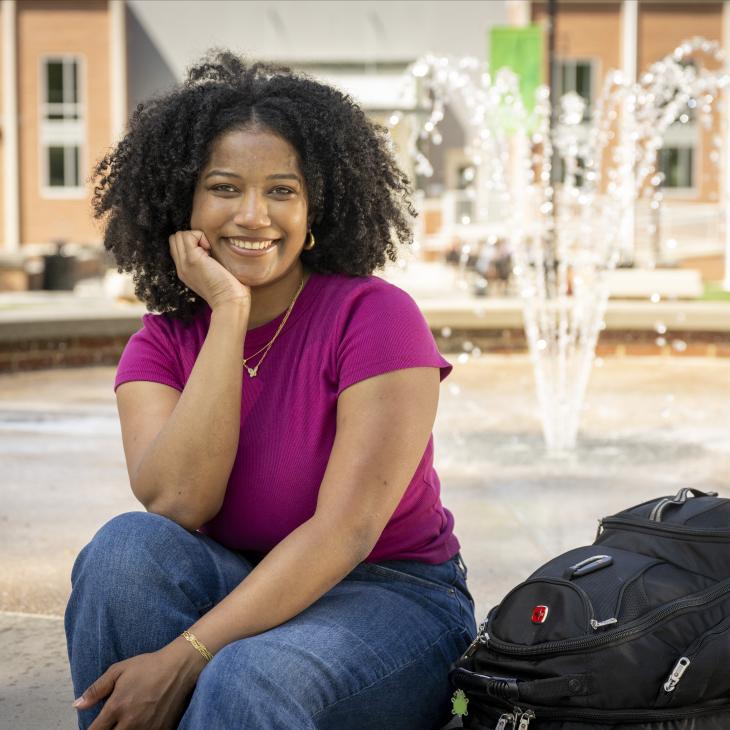 A smiling student sits by the fountain on York College campus