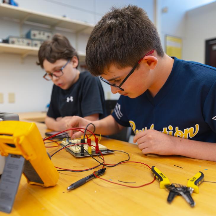 Students work on an electronics project with wires and testing equipment in a lab.