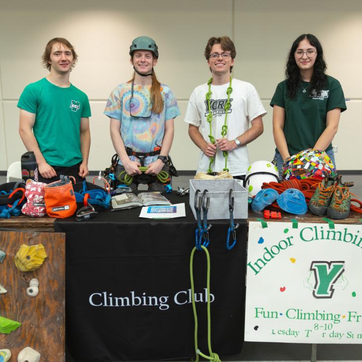 Four students stand behind a table covered in climbing equipment and a sign that says climbing club.