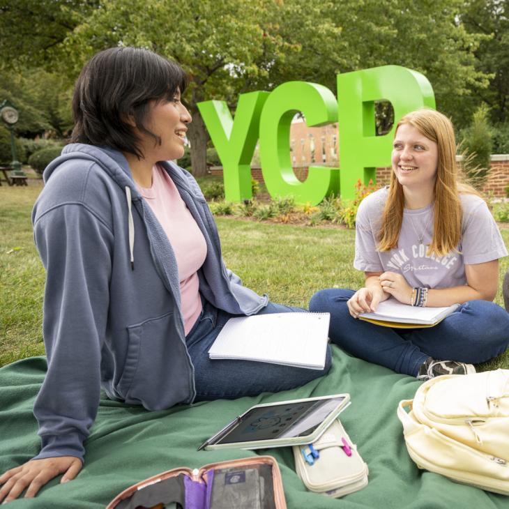 Two Students studying outside at the YCP letters.