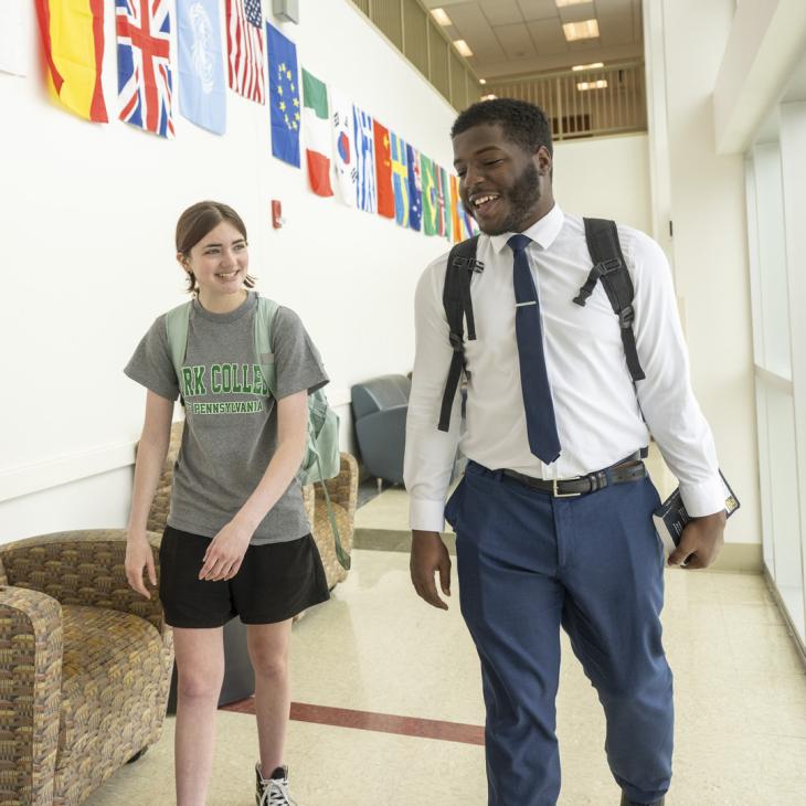 Two students walk together in a building with flags behind them.